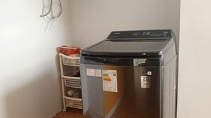Una lavadora-secadora compacta de acero inoxidable, con pantalla digital, ubicada en un rincón de una habitación con suelo de baldosas y paredes blancas.