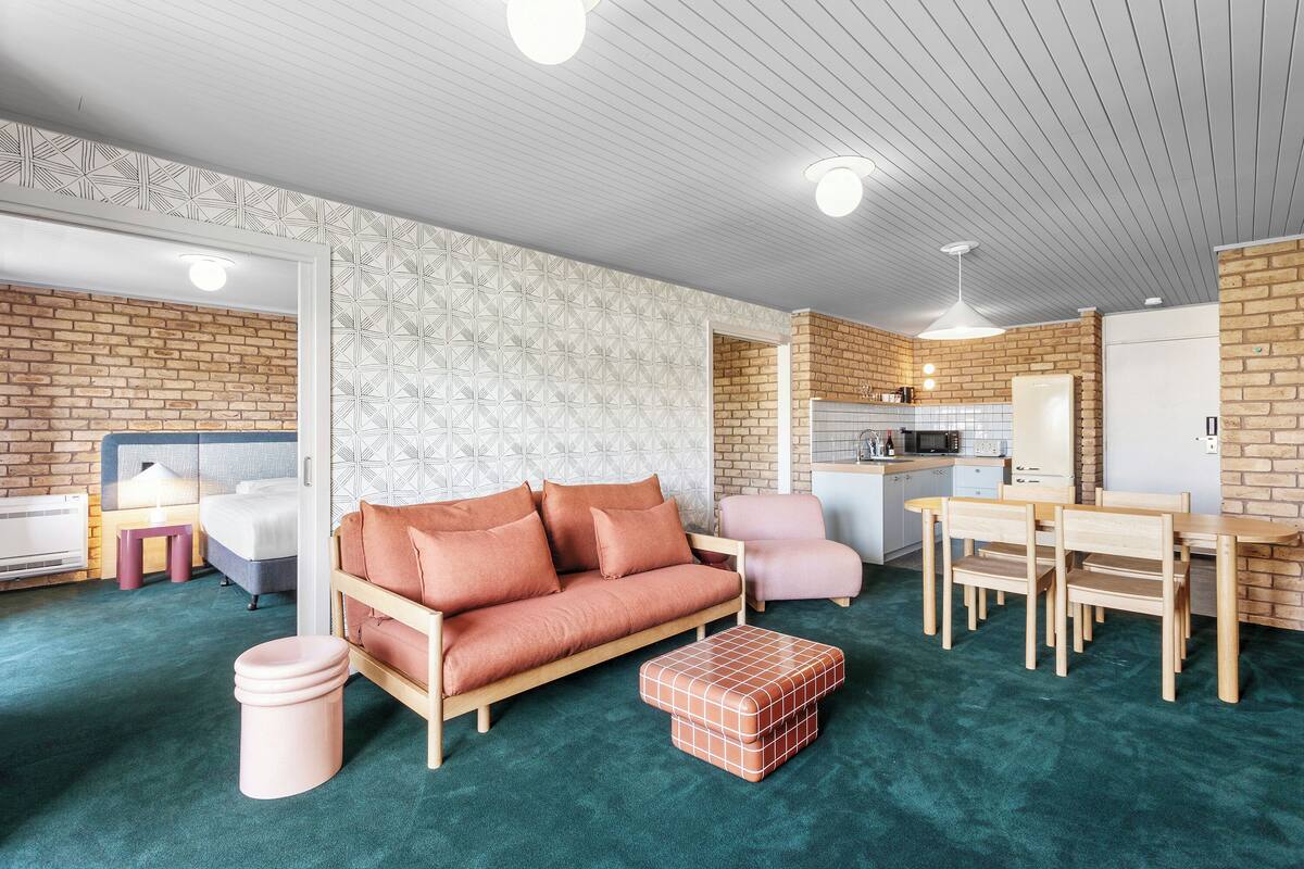 Un salon moderne avec un canapé, des fauteuils, une table basse et un coin cuisine à l’arrière-plan.