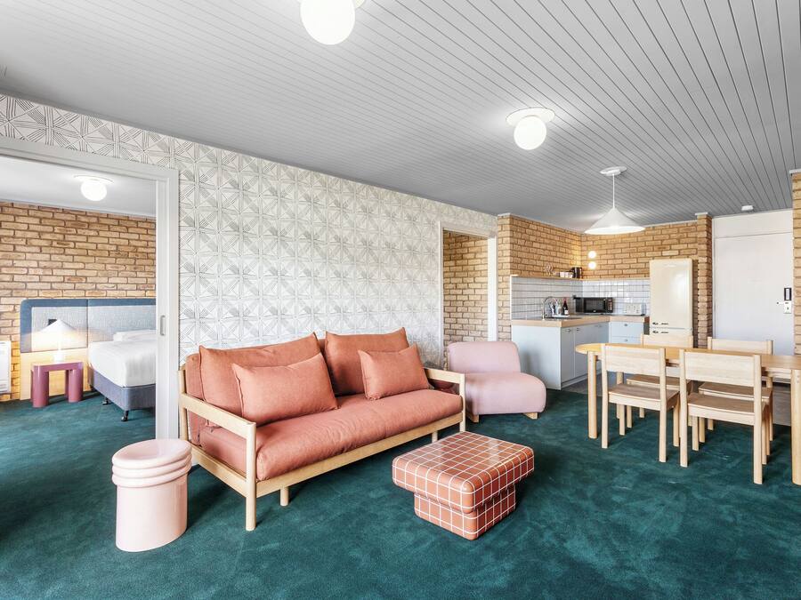 Una sala moderna con sofá, sillas, una mesa de centro y una cocina al fondo.