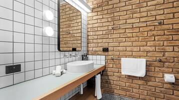 A bathroom with a white sink, a mirror, and a towel rack against a brick wall.