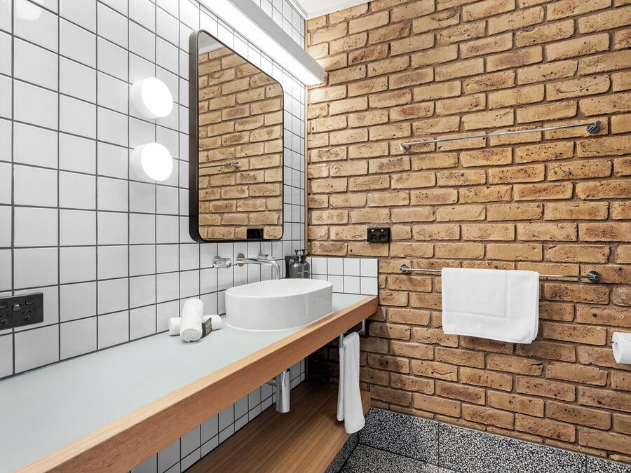 A bathroom with a white sink, a mirror, and a towel rack against a brick wall.