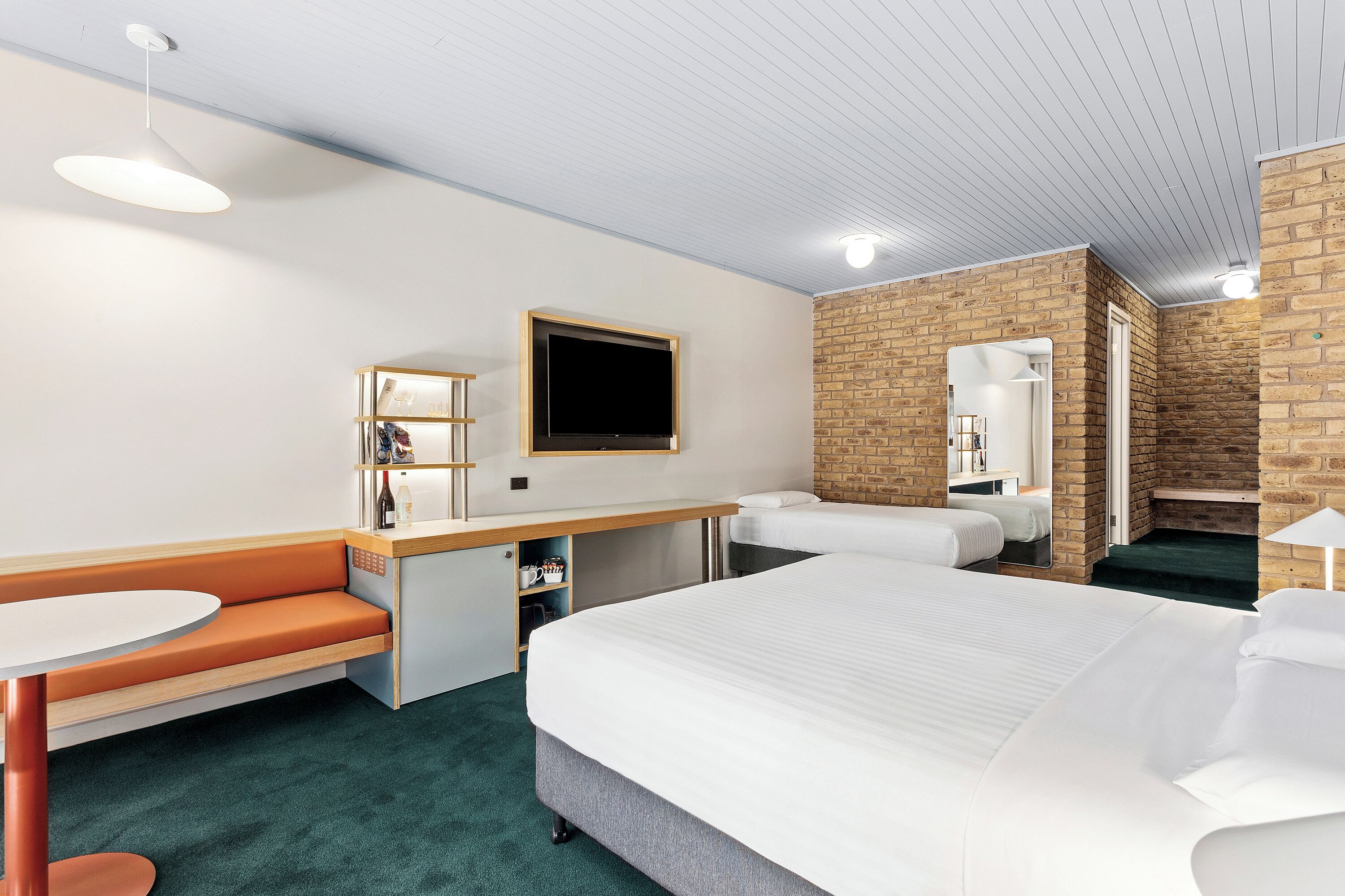 A hotel room with a large bed, a desk with a chair, a small table, a bench, and a TV on the wall.