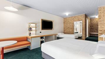 Habitación de hotel con una cama grande, un escritorio con silla, una mesita, un banco y un televisor en la pared.