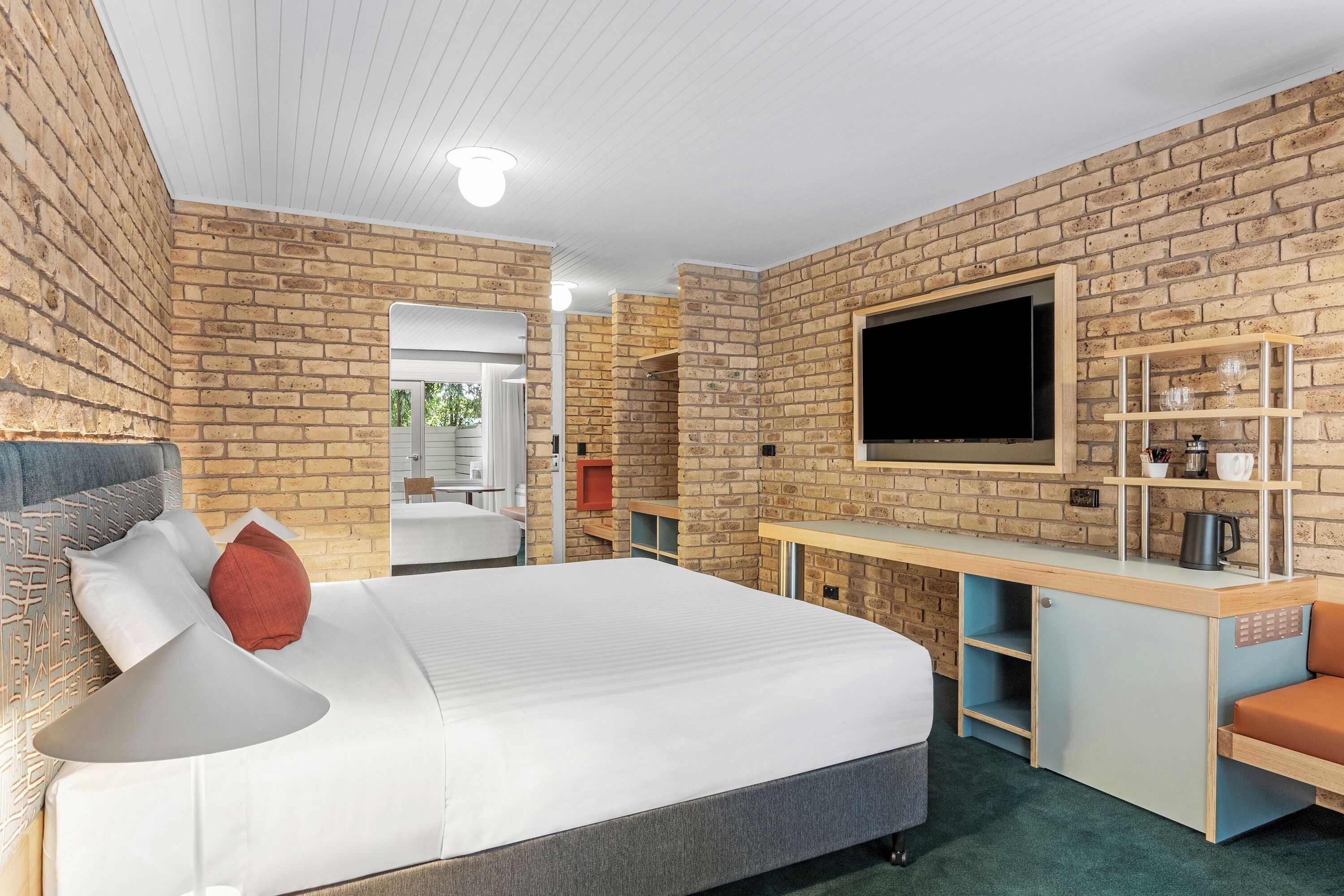A modern hotel room with a brick wall, a large bed, a TV, a desk, and a seating area.