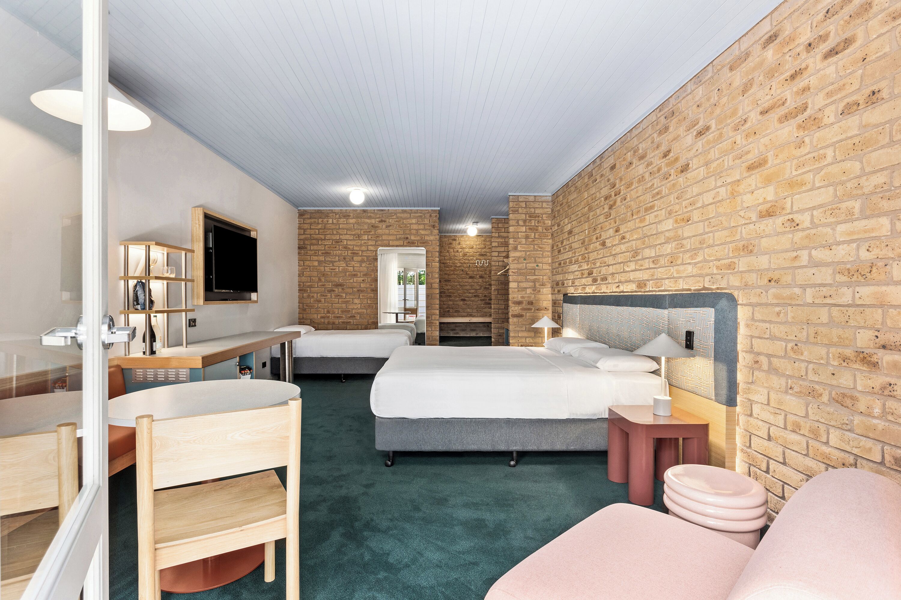 Une chambre d’hôtel avec un mur en briques, un grand lit, un bureau avec une chaise, une télévision et une salle de bain avec douche et toilettes.