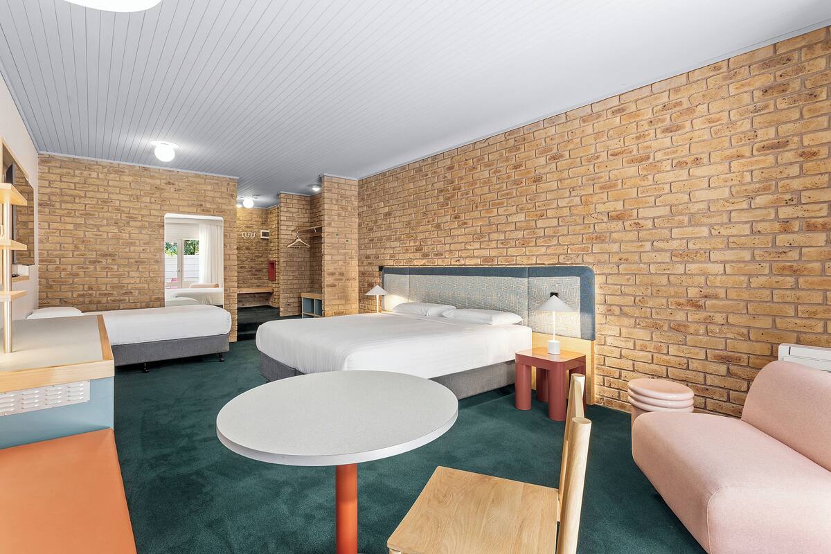 Une chambre d’hôtel avec un mur en briques, un lit, une table ronde, un canapé et une petite table avec une lampe.