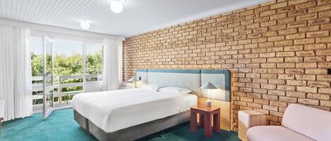 Un dormitorio con una cama grande, una pared de ladrillo, techo de madera y vistas al exterior con vegetación.