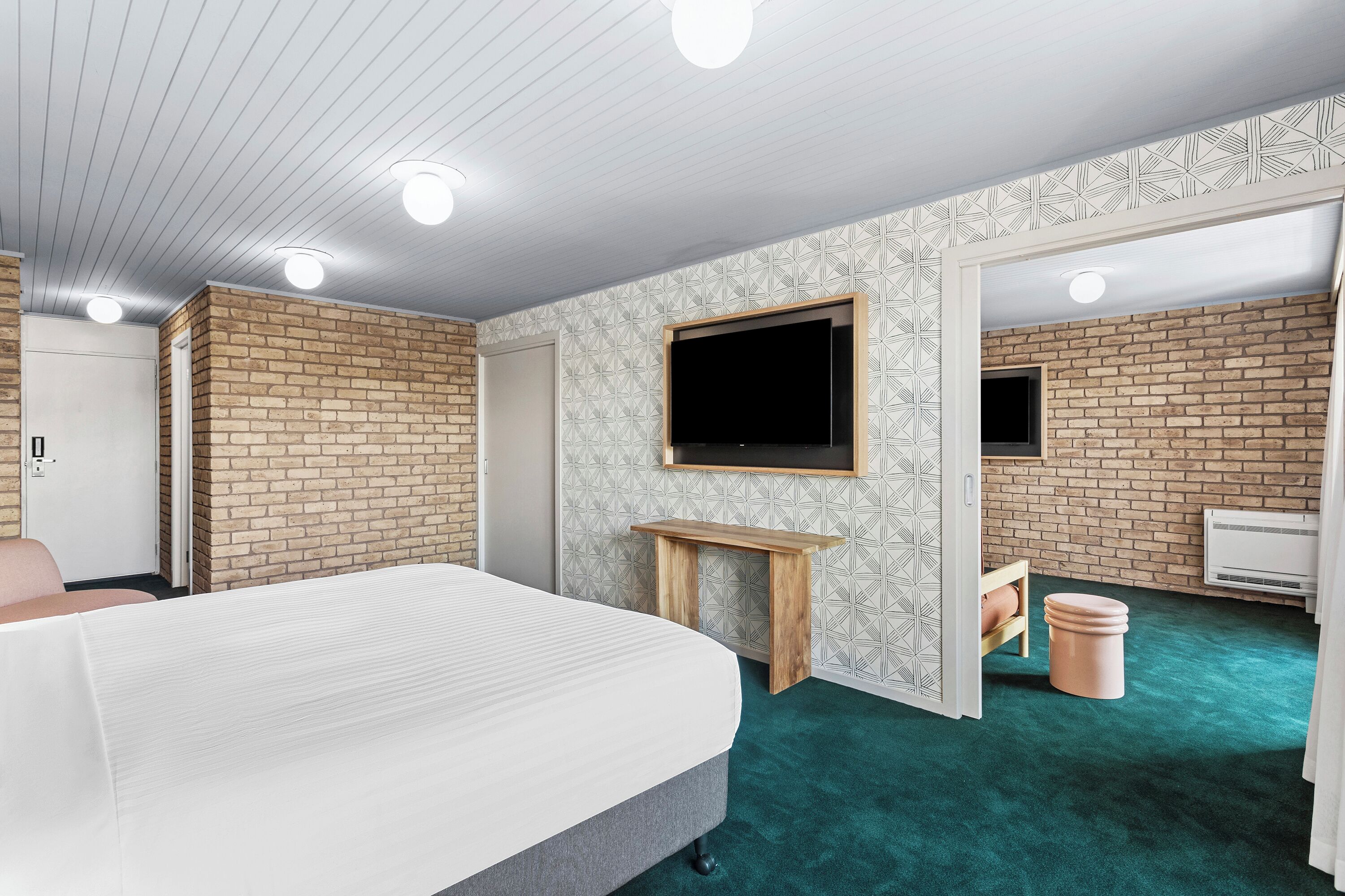 Ein Schlafzimmer mit einem Bett, einem an der Wand befestigten Fernseher, einem kleinen Holztisch und einem Mülleimer.