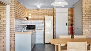 A compact kitchen with white cabinets, a refrigerator, and a dining area with wooden chairs and a table. - Motel Flinders (Flinders)
