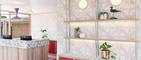 A modern reception area with a wooden counter, red cabinets, and a geometric patterned wall.