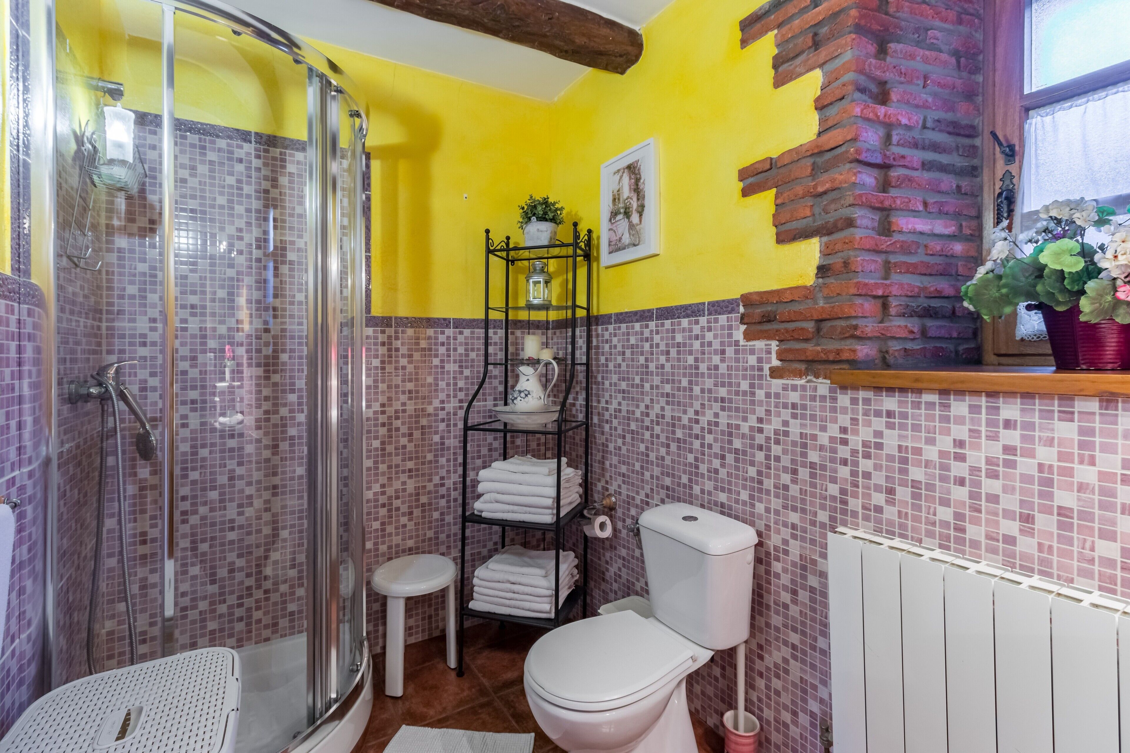 Une salle de bain équipée d’une douche, de toilettes et d’un lavabo, avec des murs carrelés et un plafond avec poutre en bois.