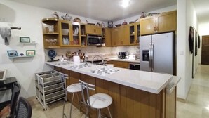 Una cocina con armarios de madera, microondas, refrigerador y una zona con taburete de bar.