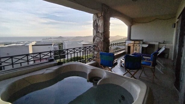 Un balcón con jacuzzi, mobiliario exterior y un pilar de piedra.