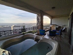 A balcony with a hot tub, outdoor seating, and a stone pillar. - Charming 2-bedroom condo with jacuzzi in Cabo San Lucas (Cabo San Lucas)