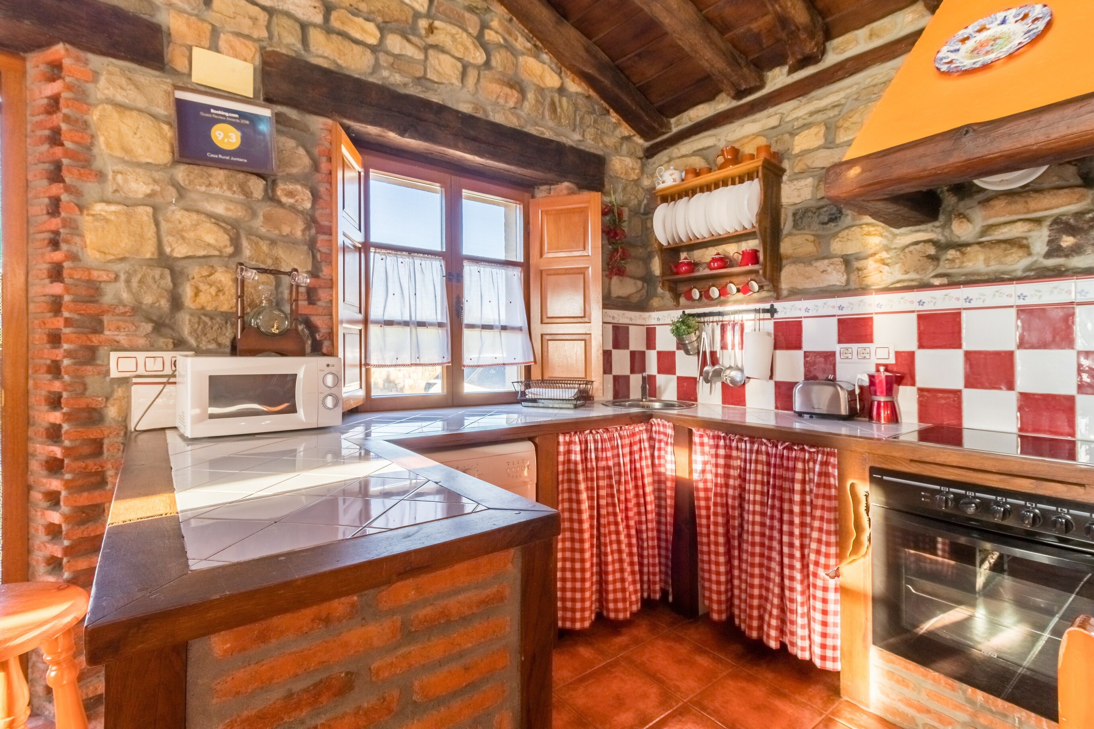 Una cocina rústica con paredes de piedra, salpicadero a cuadros, una isla de madera, un microondas, una estufa y una ventana con cortinas.