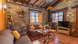 A cozy living room with a stone wall, wooden beams, a sofa, a coffee table, and a television.