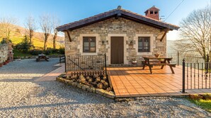 Une maison en pierre avec un patio carrelé, deux fenêtres, une porte et une cheminée.