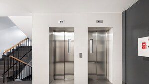 Un ascensor moderno con pantalla digital, una escalera con barandillas de madera y una pared lisa.