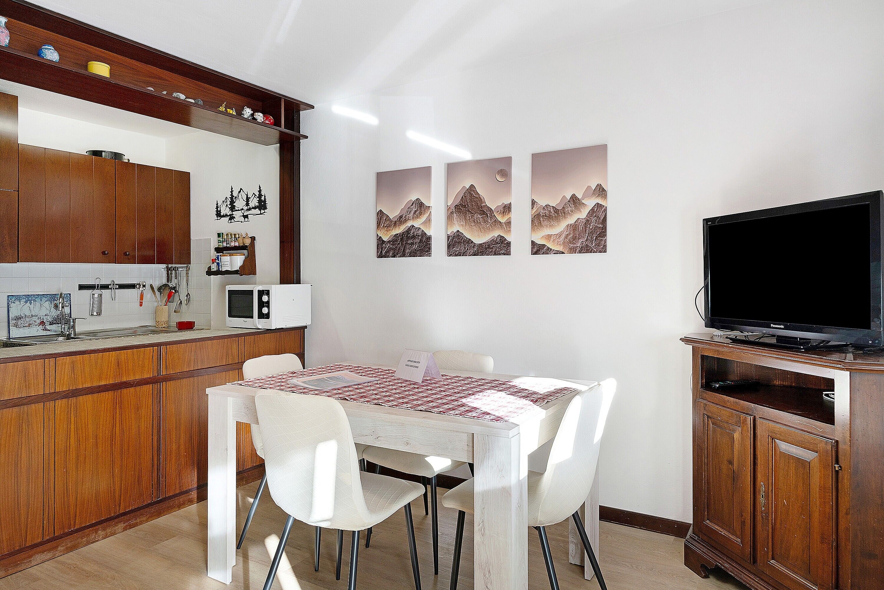 A dining area with a wooden table, white chairs, a TV, and a microwave.