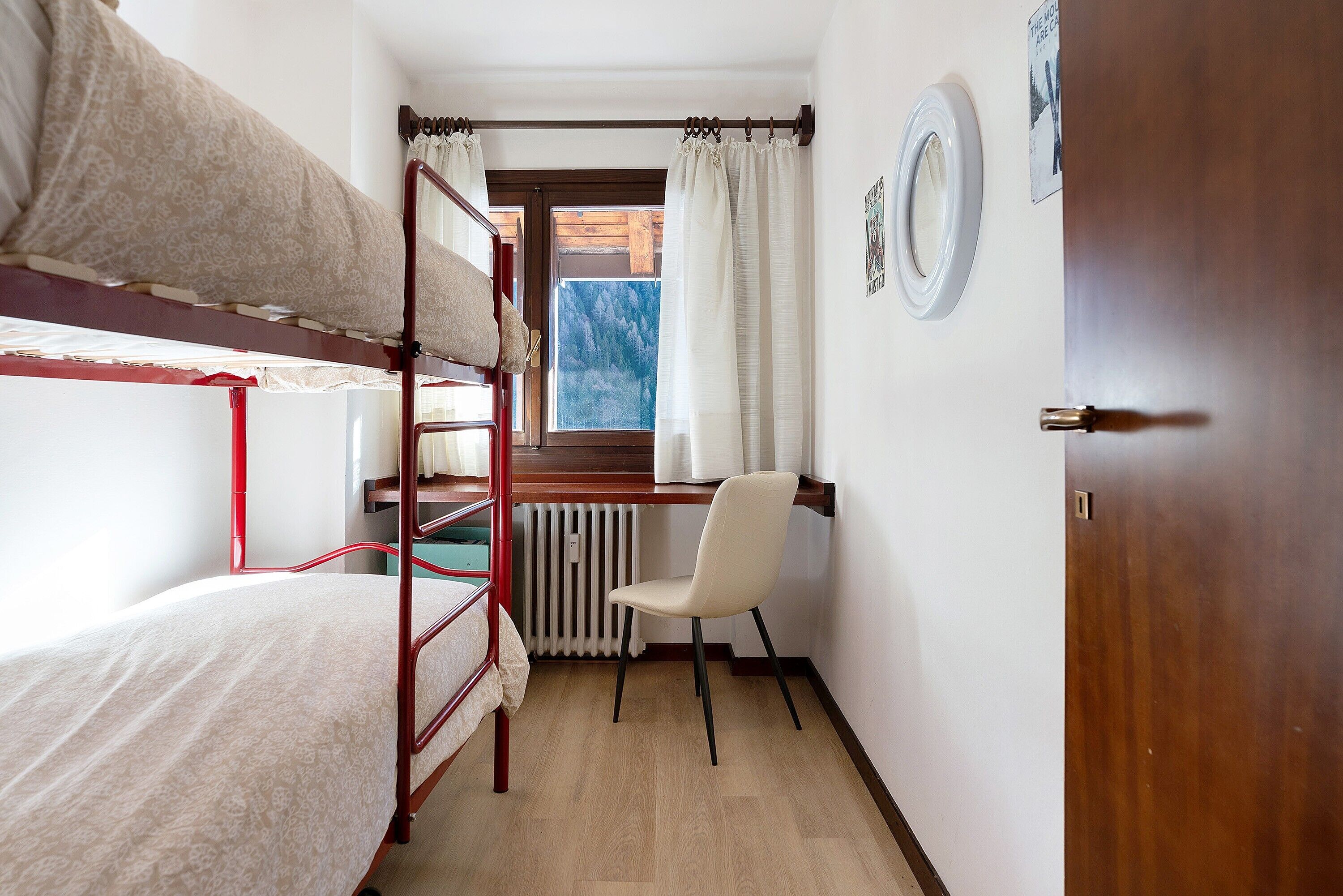 A room with bunk beds, a desk, a chair, a radiator, and a window with curtains.