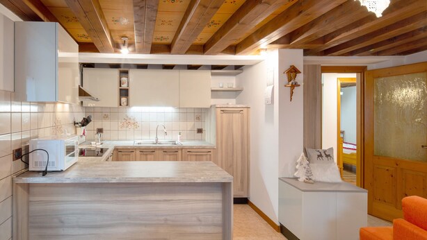 A kitchen with wooden beams, white cabinets, a marble countertop, and a small seating area with chairs. - Apartment 'Zopel' with Mountain View, Shared Garden and Wi-Fi (Falcade)