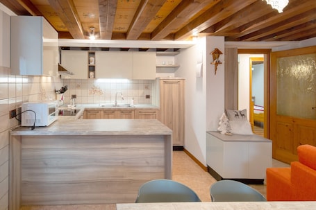 A kitchen with wooden beams, white cabinets, a marble countertop, and a small seating area with chairs.
