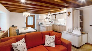 A modern kitchen with wooden beams, a dining area with a sofa, and a small table. - Apartment 'Zopel' with Mountain View, Shared Garden and Wi-Fi (Falcade)