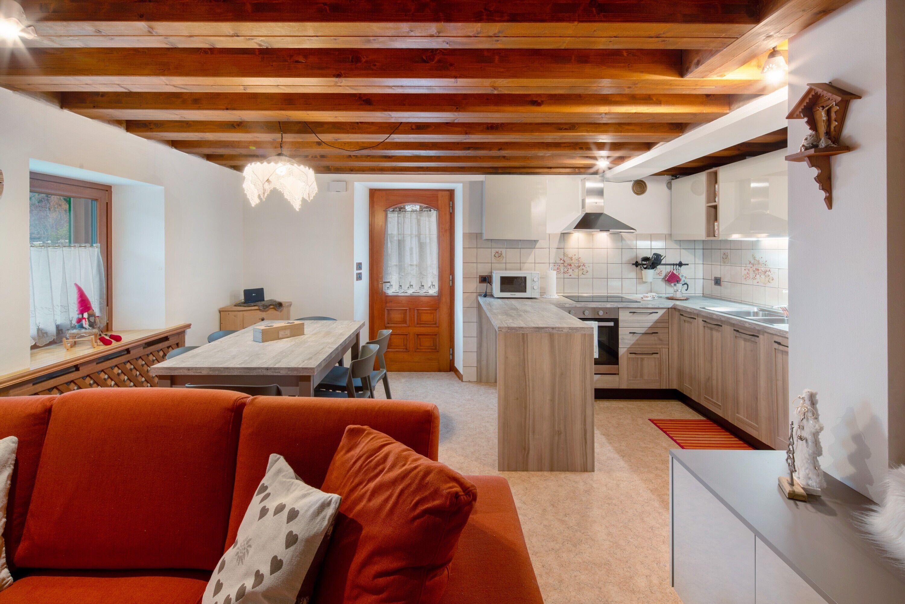 A cozy living room with a sofa and a dining area, a kitchen with wooden cabinets and a microwave, and a wooden ceiling.