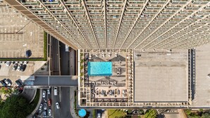 Un hotel de altura con piscina en la azotea, varios pisos y un área de estacionamiento.