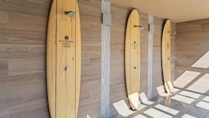 Varias tablas de surf de madera colgadas en una pared, con suelo de madera y techo de color claro.