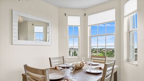 A dining area with a wooden table set for four, large windows with blinds, and a mirror on the wall.