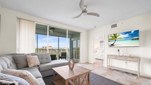 A modern living room with a sofa, coffee table, and a TV displaying a beach scene.