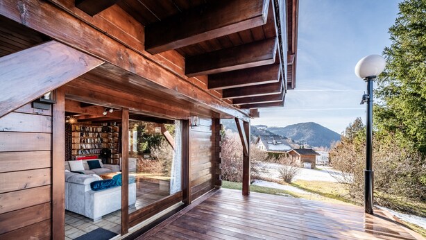 A wooden deck with a sofa and bookshelves, a view of mountains, and a satellite dish. - Chalet 'Des Charmes' with Mountain Views, Private Terrace, and Wi-Fi (Thollon-les-Mémises)