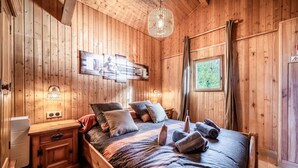 A wooden room with a bed, a wall-mounted light fixture, and a window with curtains. - Chalet 'Des Charmes' with Mountain Views, Private Terrace, and Wi-Fi (Thollon-les-Mémises)