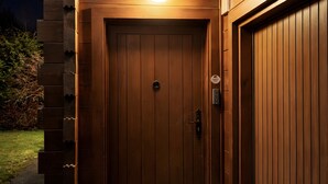 A wooden door with a peephole and a light above it, leading to a covered entrance. - Chalet 'Des Charmes' with Mountain Views, Private Terrace, and Wi-Fi (Thollon-les-Mémises)