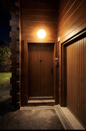 Puerta de madera con mirilla y una luz encima, que da a un acceso cubierto.