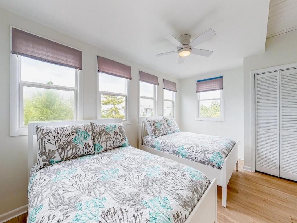Une chambre avec deux lits, un ventilateur de plafond et une fenêtre donnant sur un paysage verdoyant.