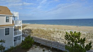 A beachfront property with a multi-story building, a sandy beach, and a clear sky.