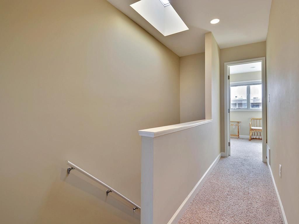 Un couloir avec une rambarde blanche, un luminaire au plafond et une porte donnant sur une pièce avec une fenêtre.