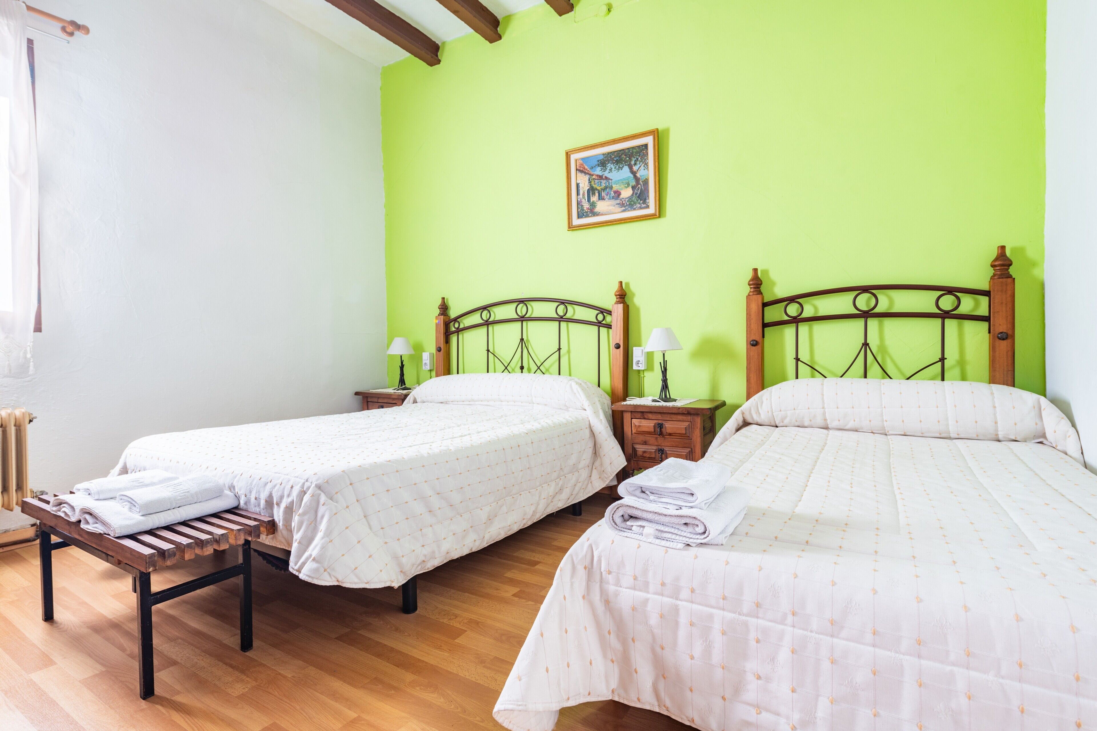 Una habitación con dos camas, bancos de madera, un radiador y un cuadro enmarcado en la pared.
