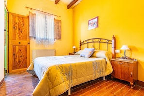 A bedroom with a bed, bedside tables, a wooden wardrobe, a radiator, and a window with curtains. - Country House 'Vell' with Mountain View, Private Garden and Wi-Fi (Cati)