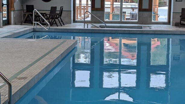 An indoor swimming pool with clear water, a diving board, and a view of the outside through large windows. - Cozy 3-bedroom/3-bathroom Townhouse, minutes from Loon Mt with an indoor pool (North Woodstock)