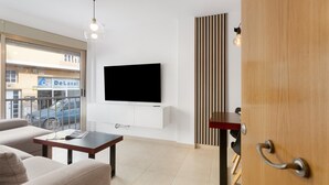 Ein modernes Wohnzimmer mit Flachbildfernseher, einer Couch, einem Couchtisch und Blick ins Freie.