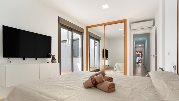 Ein modernes Hotelzimmer mit einem großen Bett, einem Flachbildfernseher, einem Kleiderschrank und einer Schiebetür zu einem Badezimmer.