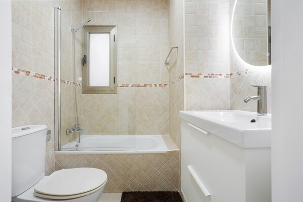 A bathroom with a toilet, a bathtub, a sink, and a mirror.