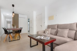 A modern living room with a sofa, a coffee table, a dining table with chairs, and a pendant light.