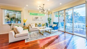 A spacious living room with a sofa, coffee table, and chairs, large windows, and a view of the outdoors. - StayAU Pakenham Townhouse with Lakeview (Pakenham)