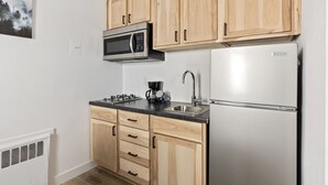 Eine kompakte Küche mit Holzschränken, einer Edelstahl-Mikrowelle, einem Kühlschrank, einem Gasherd und einer Kaffeemaschine.