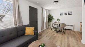 Ein modernes Wohnzimmer mit einem grauen Sofa, einem runden Couchtisch und einem Essbereich mit Tisch und Stühlen.