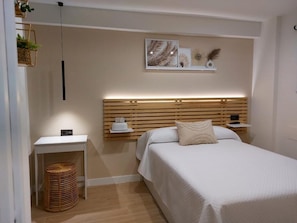 A modern bedroom with a wooden headboard, a bedside table with a lamp, and a wall-mounted shelf with decorative items.